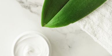 A green leaf, a white towel, and a container of cream on a marble surface.