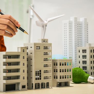 Person pointing at a model of buildings with a pen, symbolizing urban planning.