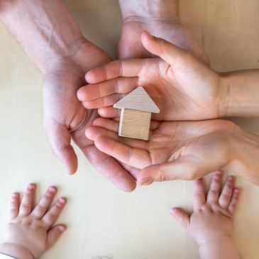 Hands holding a small wooden house model.
