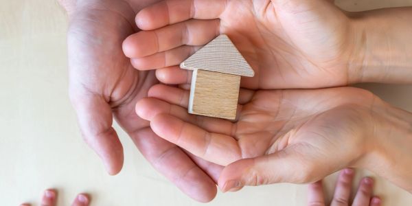 Adult and child hands holding a wooden house symbol.