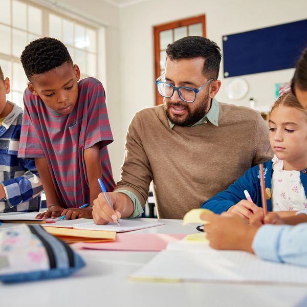 Teacher helping students with their schoolwork at a classroom table.