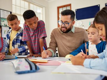 Teacher helping diverse students with classwork in a bright classroom.