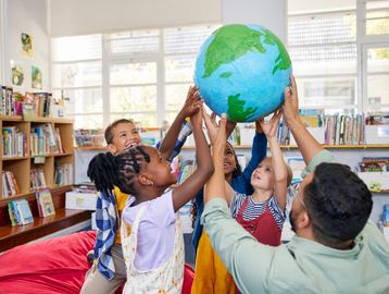 Children and a teacher holding up a globe in a bright classroom.