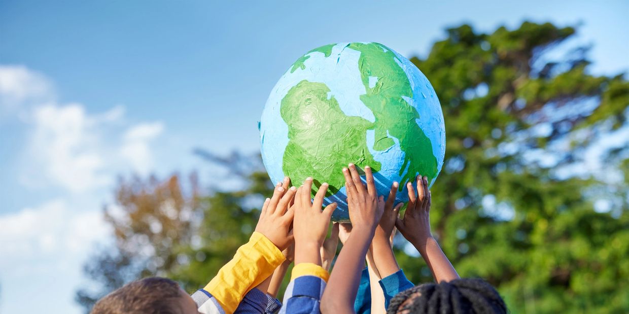 Children of diverse backgrounds holding up a globe outdoors.