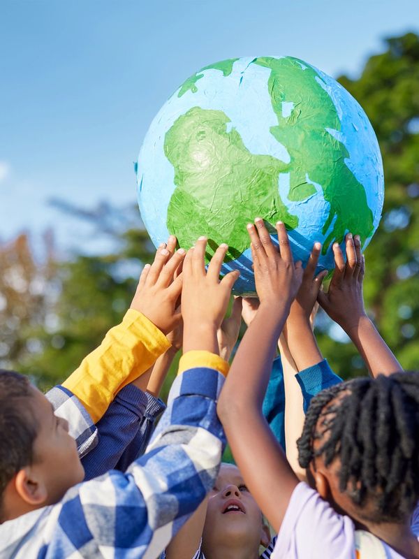 Children holding up a large globe outdoors.