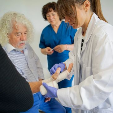 Doctor bandaging elderly man's hand in clinic.