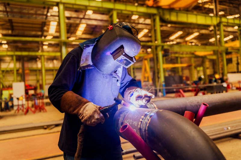 Male welder wearing helmet working with welding torch in factory.