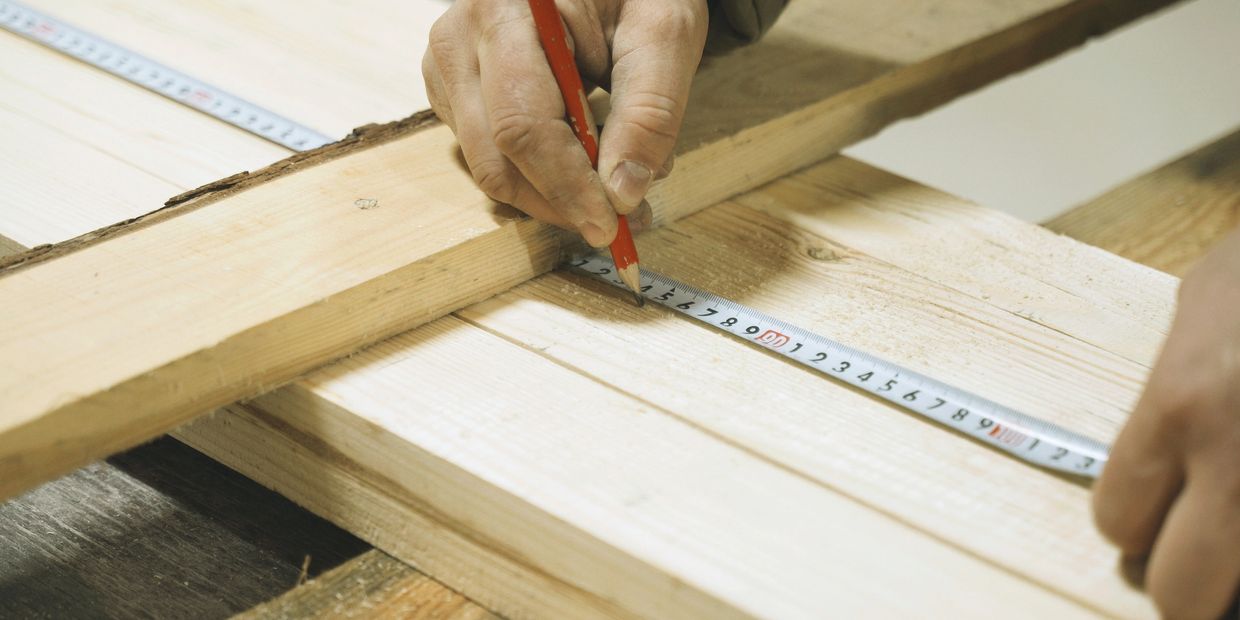 Hand marking wood with pencil and measuring tape for woodworking.