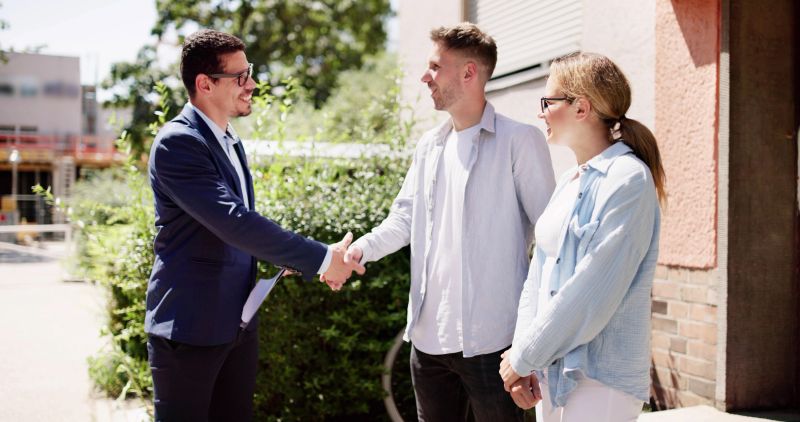Successful Real Estate Professional Celebrates Sale With Happy Young Couple In Front Of Dream Home