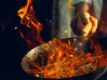 Hand stir-frying vegetables with vibrant flames in a wok.