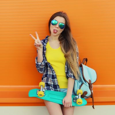 Young woman with skateboard making peace sign against orange wall.