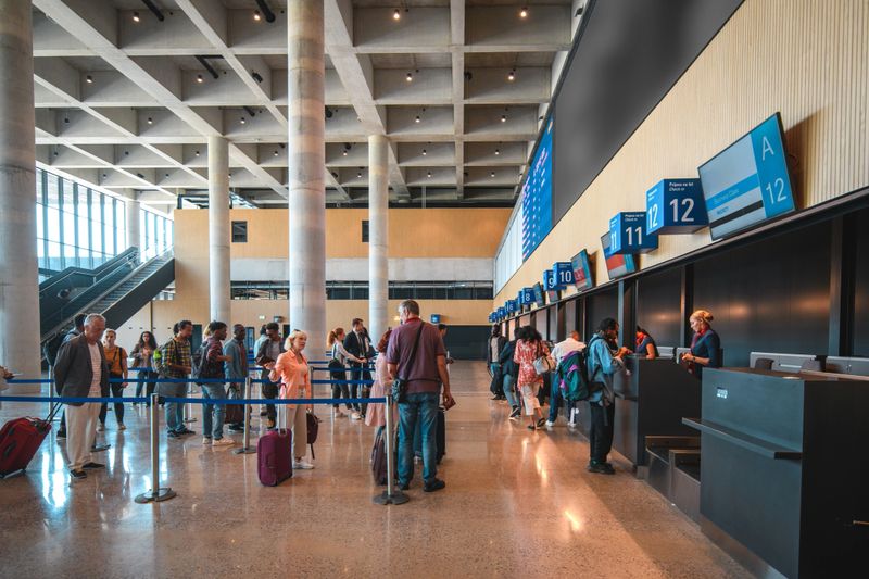 Diverse people checking in at the airport. Lining up, holding luggage and boarding passes. All wearing a protective face mask.