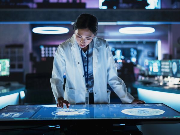 Scientist in lab coat reviewing medical imaging on interactive digital screen.