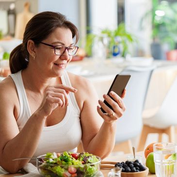 Woman enjoying a healthy salad while using her smartphone at home.