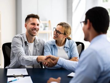 Couple shaking hands with a professional in a bright office.