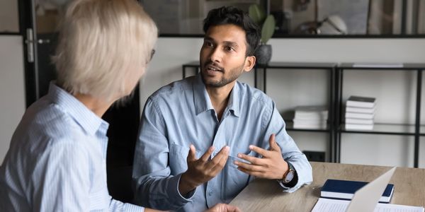 A man speaking to a woman, sat at a desk. 