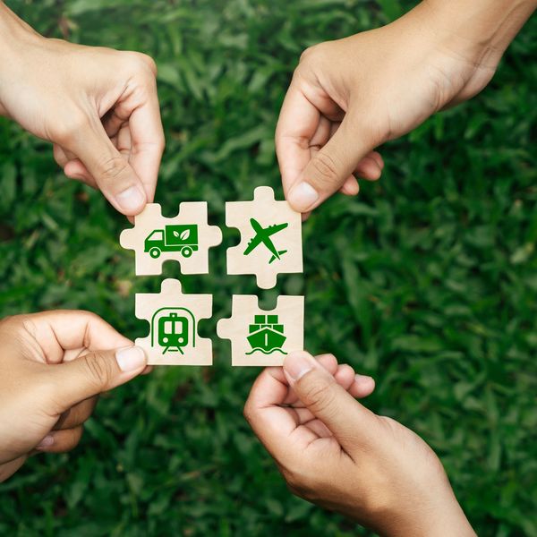 Four hands hold puzzle pieces with icons of truck, airplane, train, and ship.