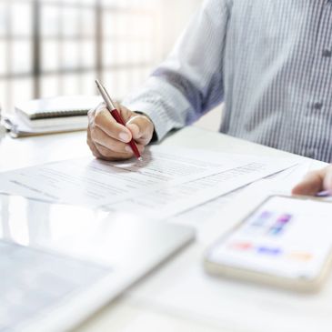 Person working at desk with documents, using a pen and smartphone.