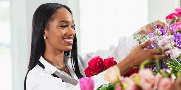 Woman arranging colorful flowers with a joyful smile.