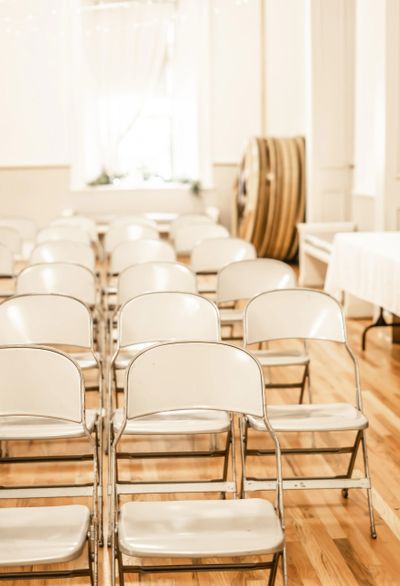 Empty white folding chairs arranged in rows on a wooden floor.