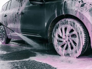 Black car being cleaned with pink foam and water spray.
