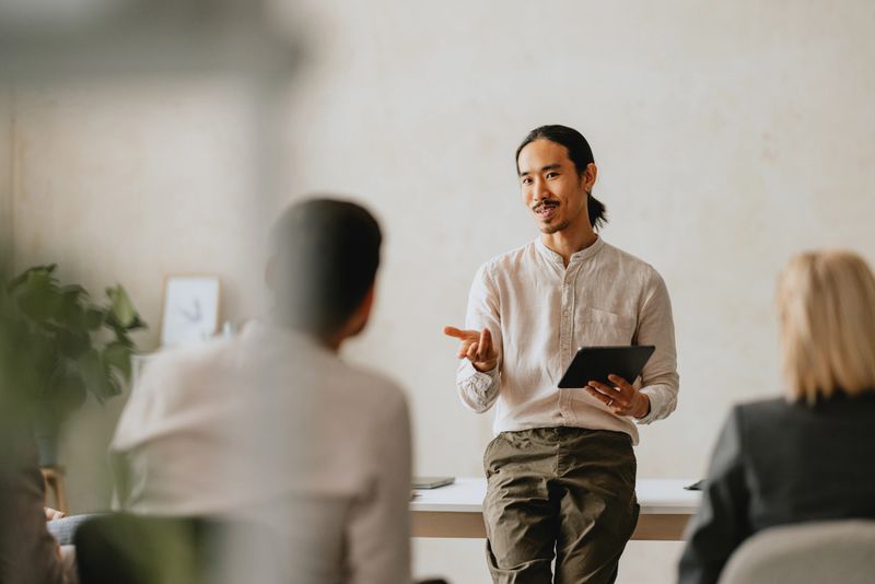 Professional man presenting with a tablet during a business meeting in a modern office. Engaged colleagues listen attentively.
