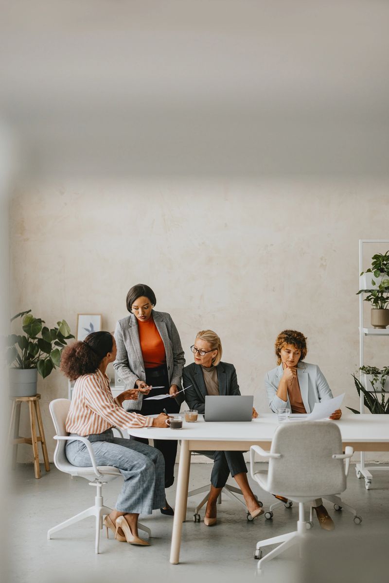 A diverse group of business professionals working together in a modern office setting, discussing documents and using a laptop.
