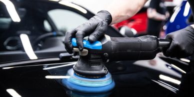 Person polishing a black car with a buffer.