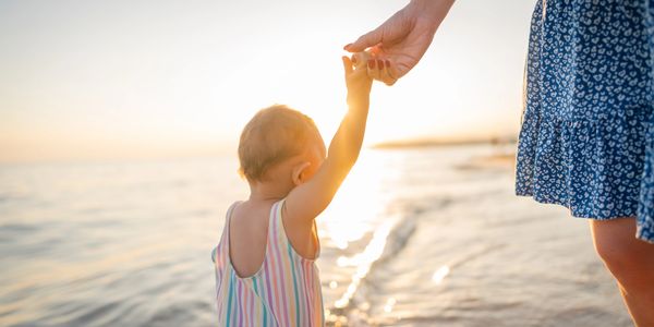 Child holding an adult's hand at the beach during sunset.