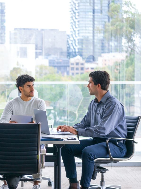 Two men having a work discussion in a modern office with city views.