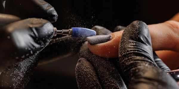 Close-up of a nail technician filing a client's nail with a rotary tool.
