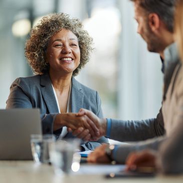 A smiling businesswoman shakes hands with a man during a meeting.