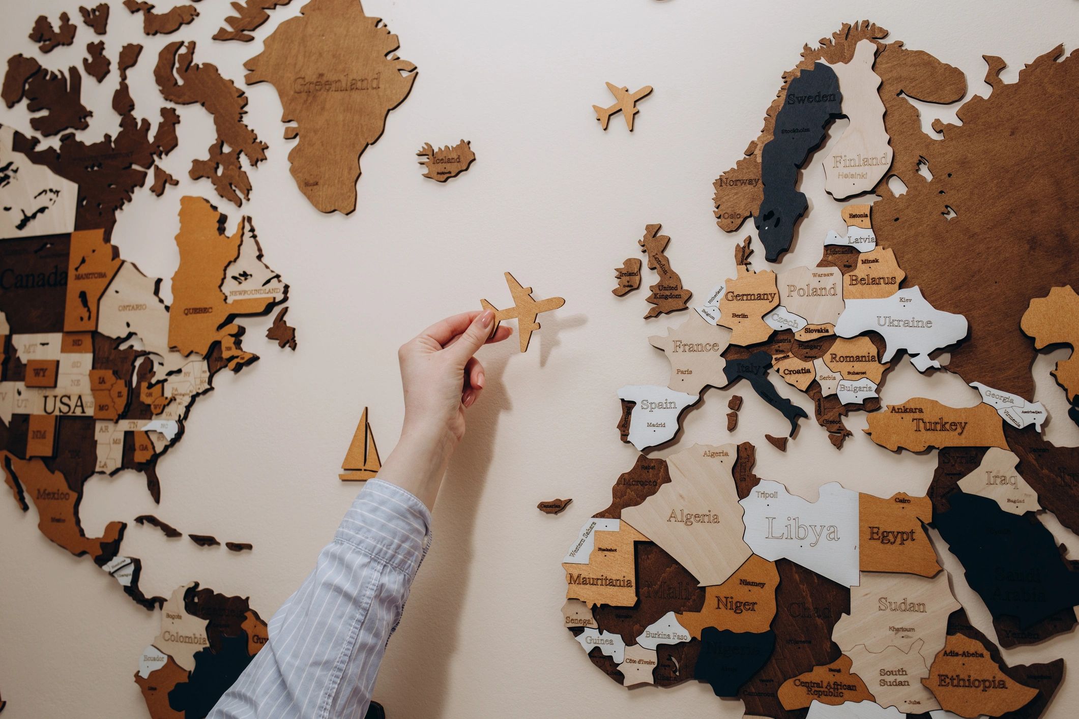 Hand holding wooden airplane over a wooden world map.