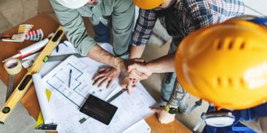 Construction workers stacking hands over blueprints.