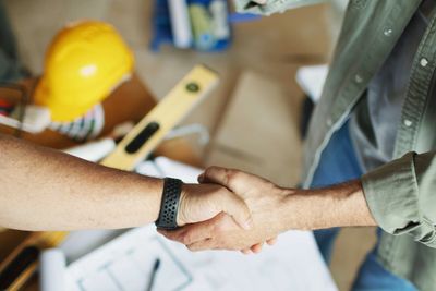 Two people shaking hands over a construction plan.