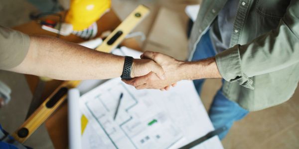 Two people shaking hands over construction plans.