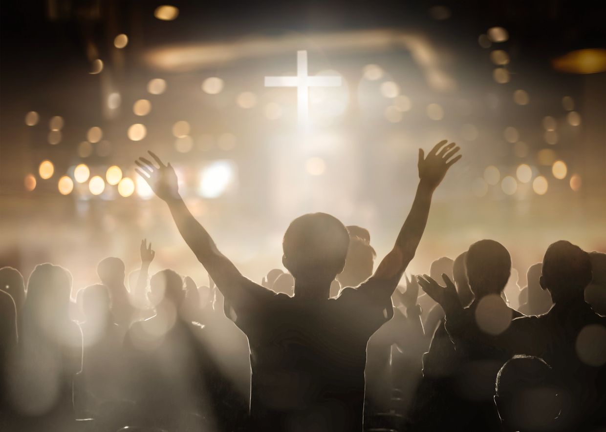 People worshipping with raised hands in front of a glowing cross.