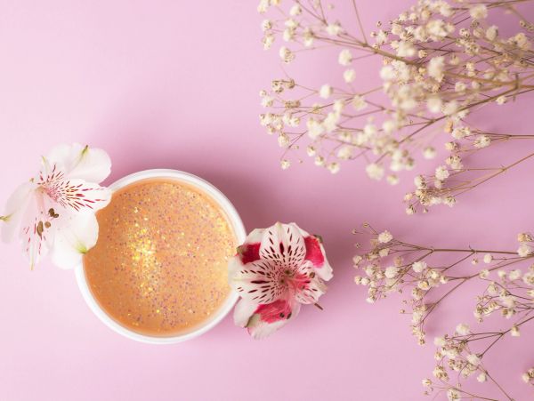 Cream jar and flowers on pink background.