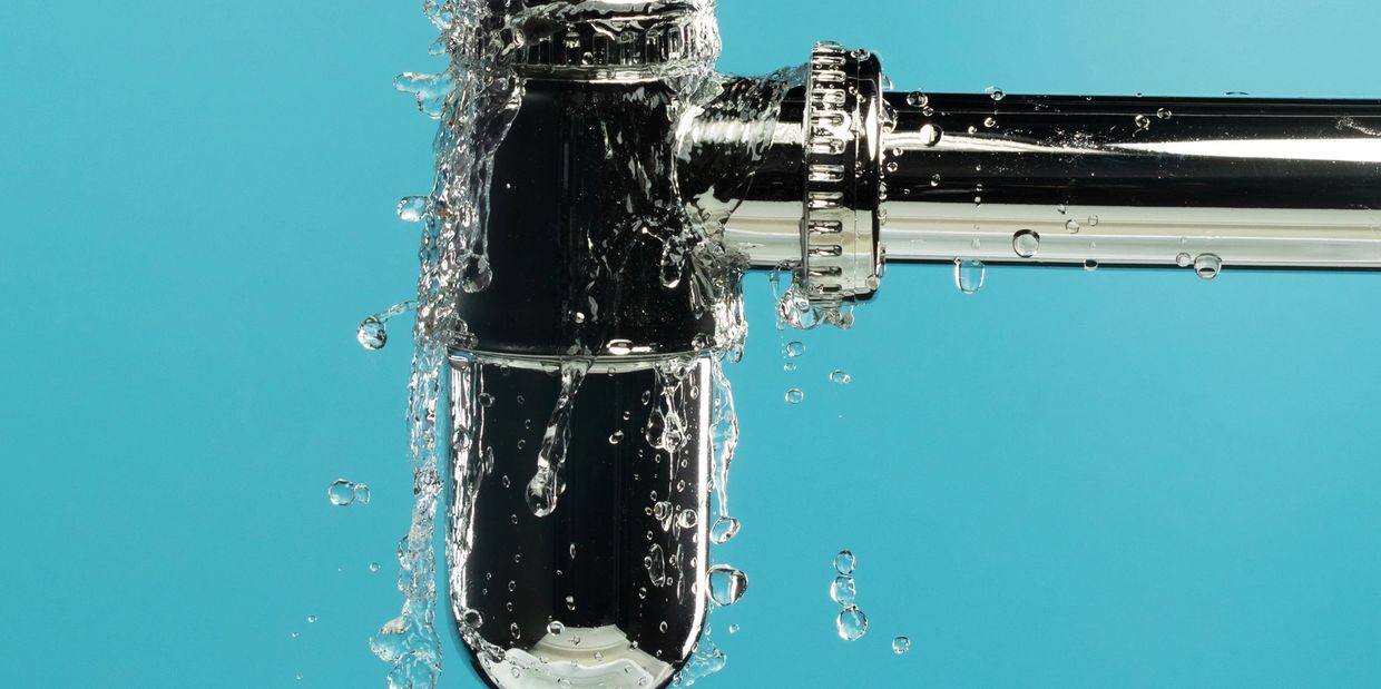 Water leaking from a chrome pipe against a blue background.