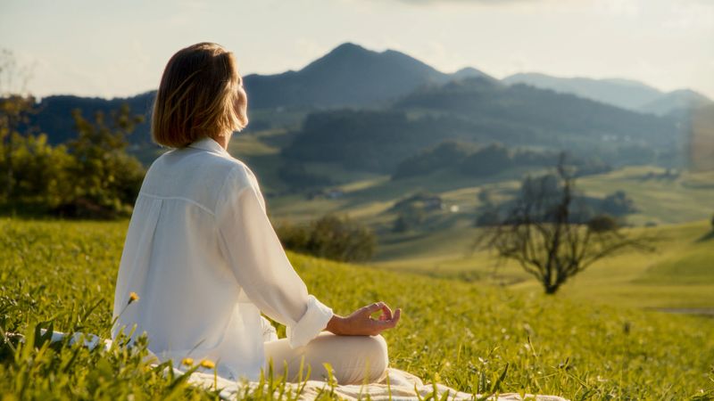 A woman enjoys peaceful meditation amidst lush greenery, dressed in casual attire, exemplifying relaxation and connection with nature.