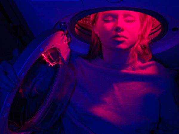 A woman with eyes closed is inside a washing machine with pink and blue lighting.
