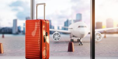 Bright red suitcase stands near airport window with plane outside.