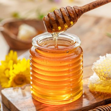 Honey dripping from a wooden dipper into a jar.