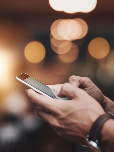 Person using smartphone with blurred lights in background.