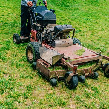 Person operating a large riding lawn mower on grass.
