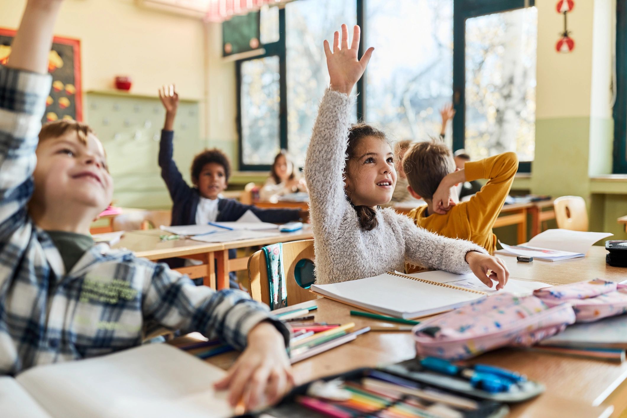 Children eagerly raising hands in a bright classroom.