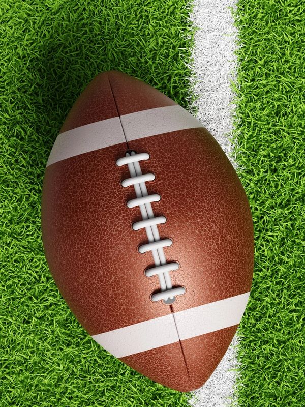 Image shows a brown football on green grass with the white out of bounds line.