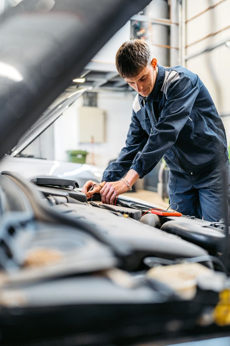 Young male car mechanic checking voltage on a car battery he is working on in his garage.