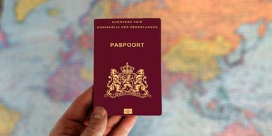Hand holding a Dutch passport with a world map background.