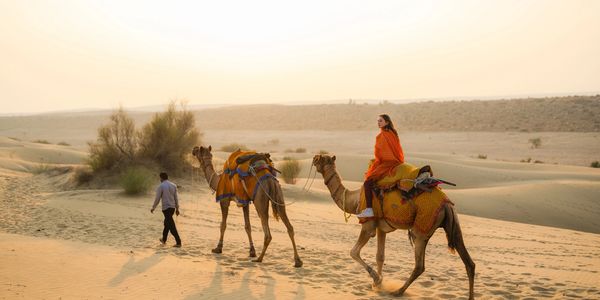 Woman riding camel in desert at sunset.